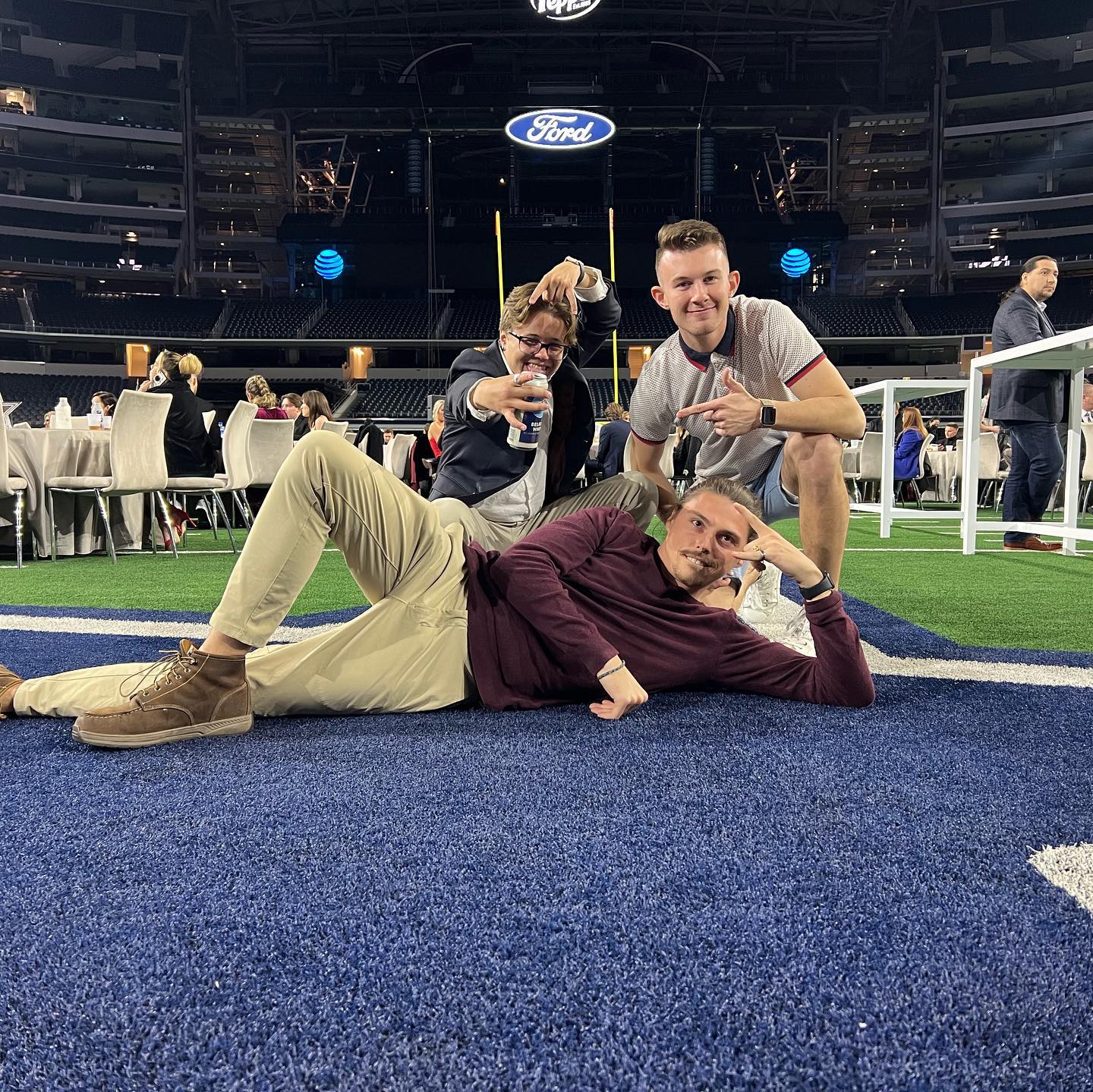 Three men standing together on a football field beneath stadium lights